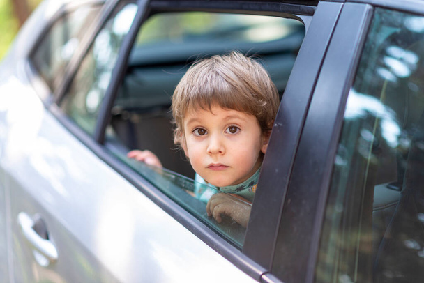 Kleiner Junge mit Kopf lehnte sich durch das offene Fenster eines Autos - Foto, Bild