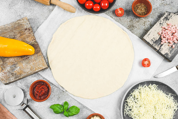 ピザの材料:チェリートマト,コショウ,チーズ,ハム,円の中にロール生地とバジルと木製のチップは、コピースペースとテーブルの上に横たわる,トップビューのクローズアップ.ピザの調理の概念. - 写真・画像