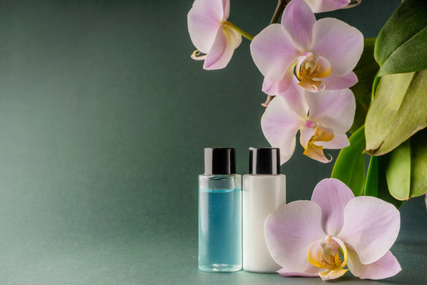 Sprchový gel a šampon v malé lahvičce, černé víčko na zeleném pozadí s orchidejí. Kvalitní fotografie - Fotografie, Obrázek