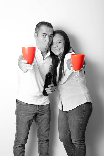 Couple d'adultes latins en noir et blanc montrent leur amour en trinquant avec des lunettes rouges pour l'arrivée de Février et de célébrer l'amour de la Saint-Valentin et de l'amitié - Photo, image