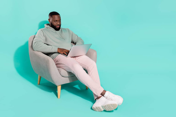 Full length body size view of handsome trendy guy sitting in armchair using laptop isolated over shine teal turquoise color background - Фото, зображення