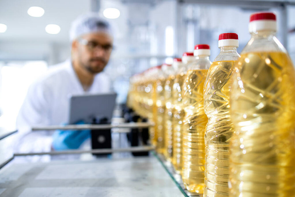 Produkcja oleju roślinnego butelkowanego w fabryce żywności i pracownik w białej powłoce z procesem kontroli siatki na włosy. - Zdjęcie, obraz