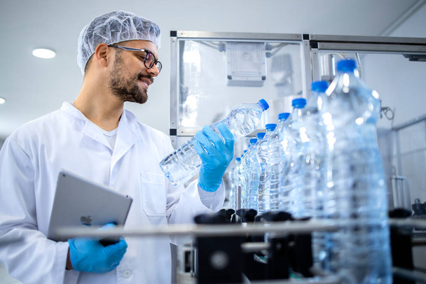 Fabrika teknisyeni şişeleme fabrikasındaki su üretiminin kalitesini dikkatlice kontrol ediyor.. - Fotoğraf, Görsel