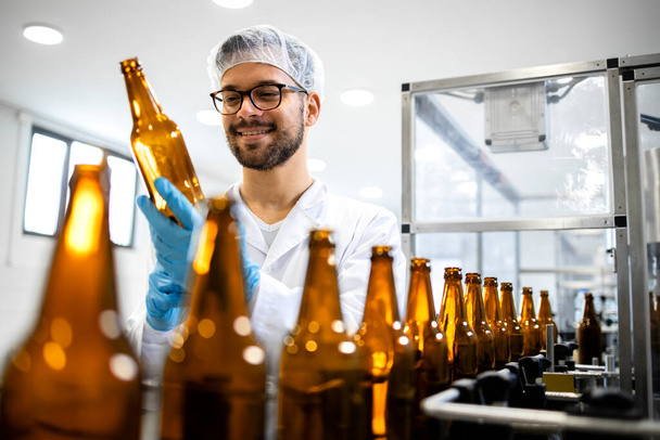 Beverage bottling factory and technologist worker checking beer bottles before filling with alcohol drink. - Fotó, kép