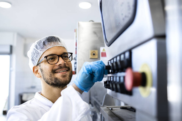 Élelmiszer-ipari dolgozó steril egyenruhában és hajhálóval működő ipari termelő gépben. - Fotó, kép