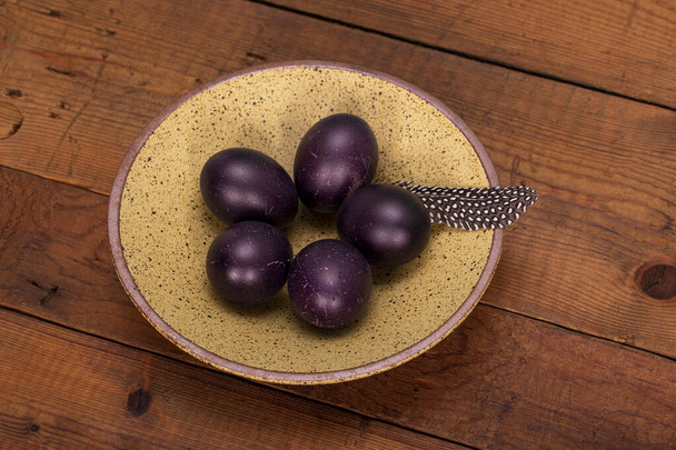 Dark violet easter eggs in a plate on a rustic wooden background - Foto, Bild