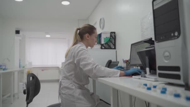 Επιστήμονας γυναίκα εργάζεται στο χώρο εργασίας της στο εργαστήριο, χρησιμοποιεί προσωπικό υπολογιστή. Ανάπτυξη, αναλύσεις και γενετική. Φαρμακευτικό Κέντρο Ερευνών. Μικροβιολόγος ελέγχει τα δεδομένα στον υπολογιστή στο εργαστήριο - Πλάνα, βίντεο