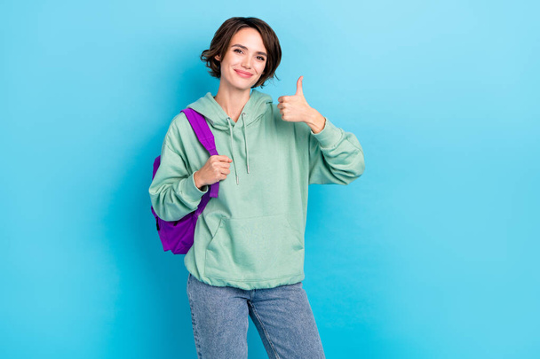 Photo of charming sweet woman wear green sweatshirt rucksack showing thumb up isolated blue color background - Foto, imagen