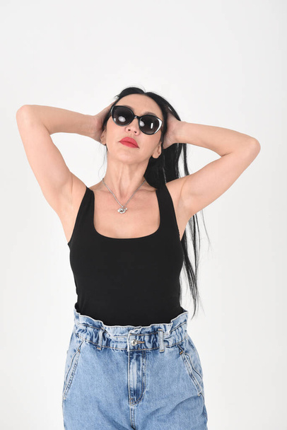 A gorgeous brunette in the studio on a white background in sunglasses corrects her hairstyle - Fotoğraf, Görsel