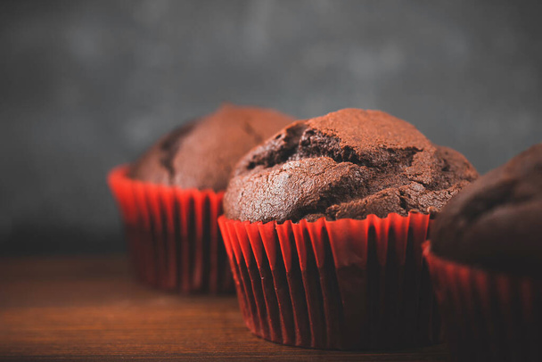 Homemade chocolate muffins or cupcakes on a wooden table and dark background. - Фото, зображення