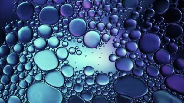 Abstrakti värikäs elintarvikeöljy tippaa kuplia ja palloja virtaa veden pinnalla, makrovideografia - Materiaali, video