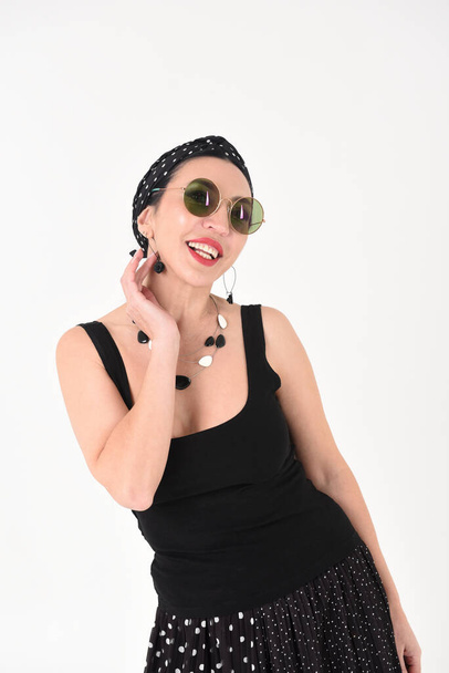 Portrait of a beautiful brunette woman in a black dress with a smile on a white background in a studio with dark glasses - Photo, Image