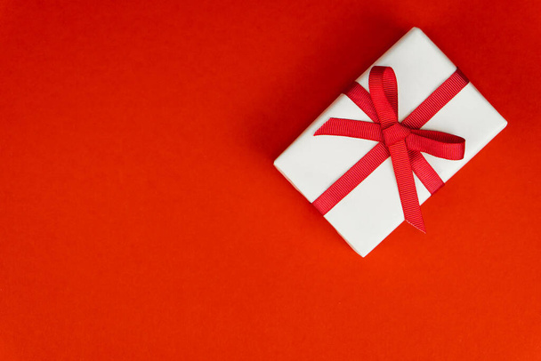 Ystävänpäivä tai syntymäpäivä konsepti kopioi tilaa. Valkoinen lahjapakkaus, jossa punainen nauha punaisella paprikalla - Valokuva, kuva