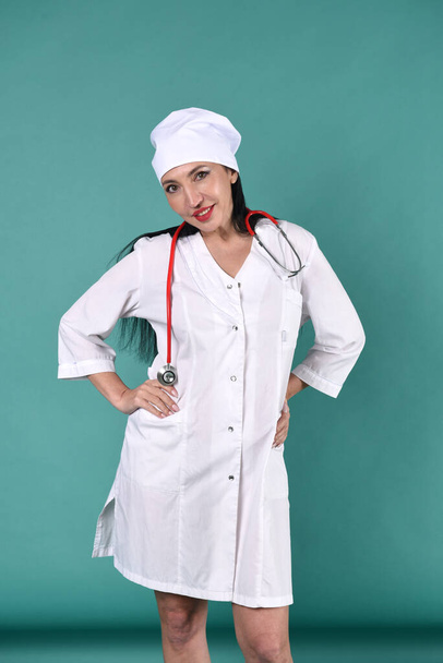 A female therapist in a white coat and a white headdress on a green background with a stethoscope - Фото, зображення