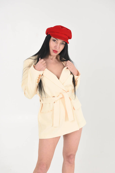 Stylish fashionable brunette woman in a yellow jacket, red cap and beautiful legs in the studio on a white background - Foto, imagen