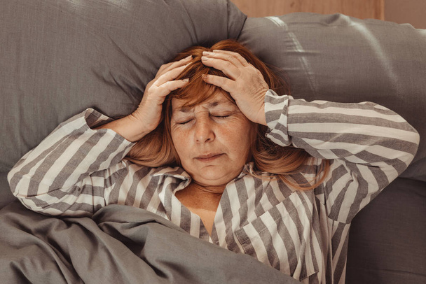 Nieszczęśliwa biała kobieta w średnim wieku źle się czuje z bólem głowy, migreną, stresem, bezsennością po przebudzeniu rano w łóżku - Zdjęcie, obraz