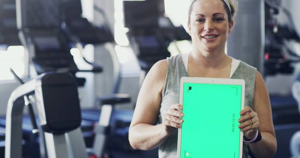 Mühelos jede Aktivität verfolgen. 4K-Video einer Frau, die im Fitnessstudio ein digitales Tablet hochhält. - Foto, Bild