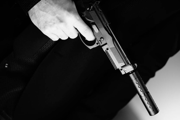 Ένας καλοντυμένος μυστικός πράκτορας ντετέκτιβ κατάσκοπος φοράει κοστούμι και γραβάτα κρατώντας αυτόματο πιστόλι.. - Φωτογραφία, εικόνα