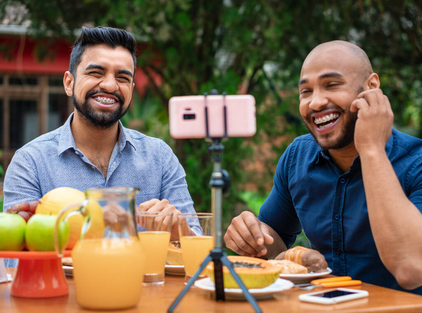 fun gay couple sitting and using mobile for video call in table outside - 写真・画像