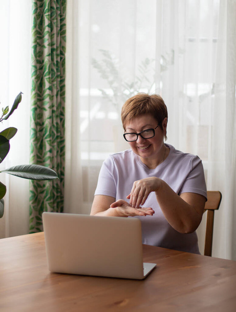 Une femme adulte est assise sur un ordinateur portable et communique par lien vidéo en langue des signes. Affiche le mot écrire par geste. - Photo, image