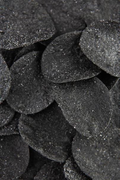 Selective focus. Macro chips. Spices and salt on black chips. Black chips with spices on a plate, cuttlefish ink food - Photo, Image