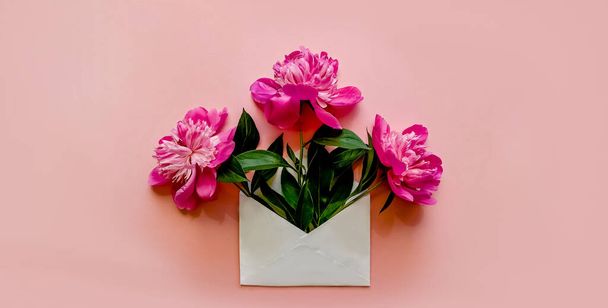 White envelope with pink peonies inside on a pink background. - Fotoğraf, Görsel