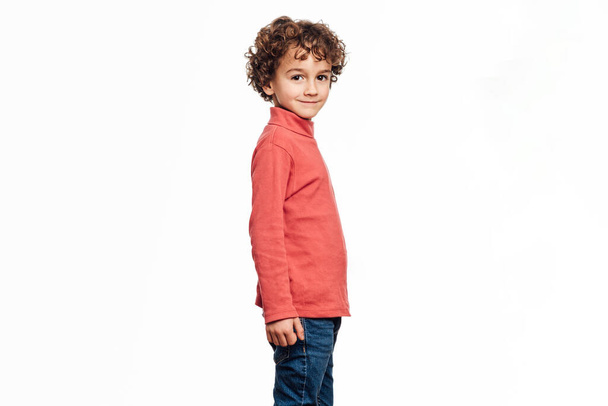 Niño mirando a la cámara y sonriendo mientras posando sobre un fondo blanco aislado. - Foto, imagen