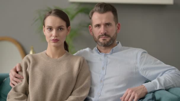 Portrét páru při pohledu na fotoaparát při sezení na pohovce  - Záběry, video