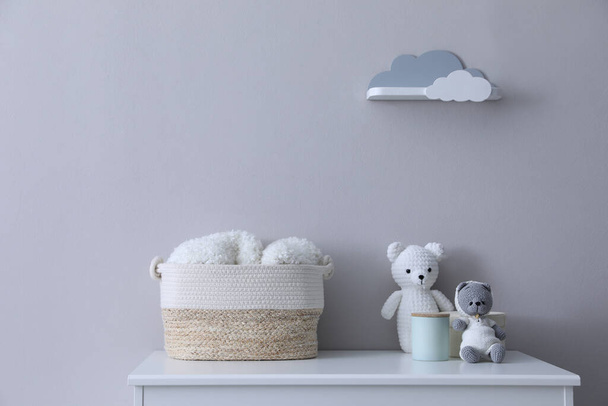 Child's toys, wicker basket and accessories on chest of drawers near light grey wall indoors - Fotoğraf, Görsel
