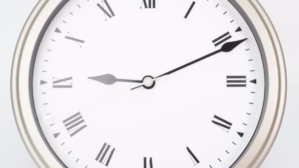 Time lapse zilveren muur klok vertelt de tijd om 10 uur. Toont het verstrijken van de tijd op Romeinse cijfers. Op witte achtergrond. - Video