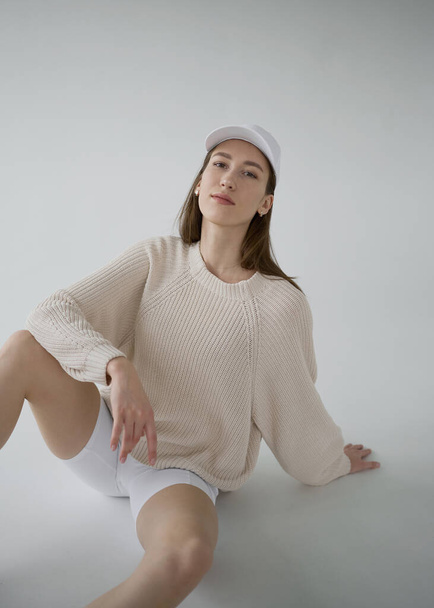 Cool sporty girl in beige sweater and white bicycle pants on neutral grey background. Soft light, monochrome picture. Good vibes, positive emotions. Tall and slim european model in good shape. - Φωτογραφία, εικόνα