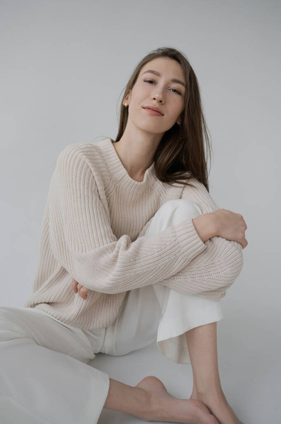 Cool sporty girl in beige sweater and white bicycle pants on neutral grey background. Soft light, monochrome picture. Good vibes, positive emotions. Tall and slim european model in good shape. - Valokuva, kuva
