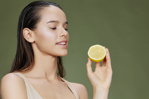 женщина с лимоном рядом с лицом чистый уход за кожей зеленый фон - Фото, изображение