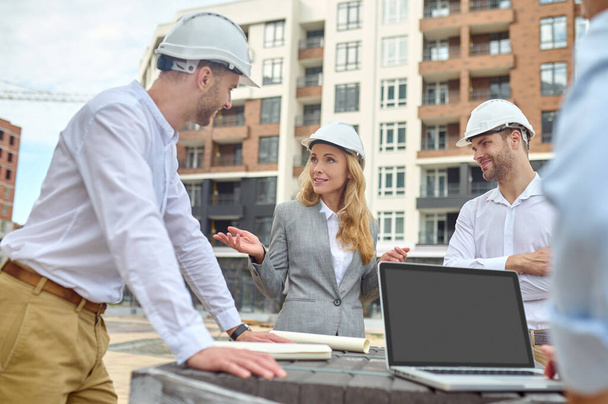 Elegant building supervisor talking to builders outside - Фото, изображение