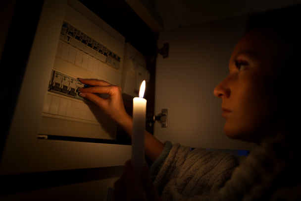 Kobieta w całkowitej ciemności badająca skrzynkę bezpiecznikową w domu podczas przerwy w dostawie prądu lub zaciemnienia. Brak koncepcji energii elektrycznej - Zdjęcie, obraz
