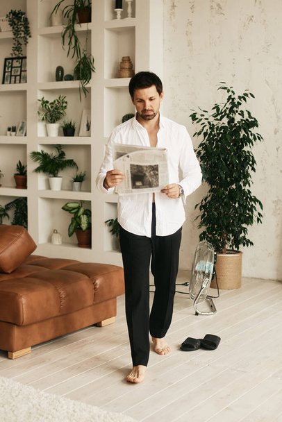European man in his flat. Sitting in the living room. Bronze skin. Dark eyes and hair. Beard. Light colored interior. Casual clothes style. Weekend at home. Domestic atmosphere. Cosiness and comfort - Foto, immagini