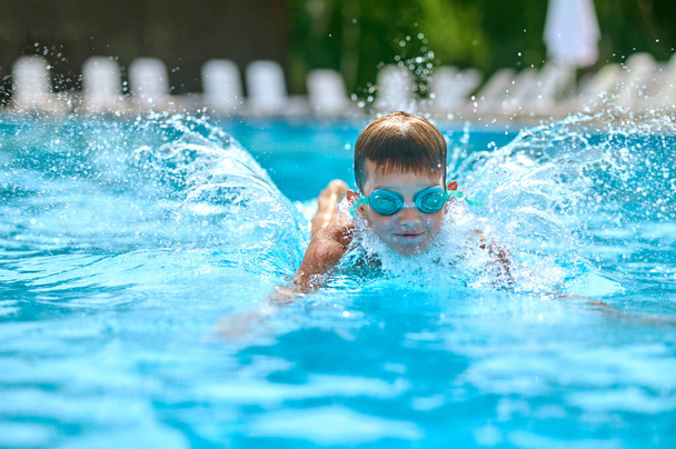 Boy in goggles swimming splashing in pool - Zdjęcie, obraz