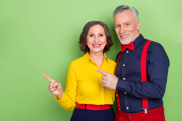 Portrait of two stylish elderly partners indicate finger empty space blank isolated on green color background - Foto, immagini