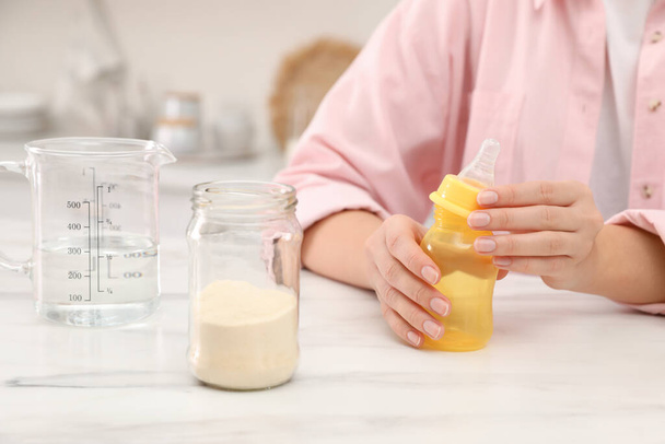 Woman preparing infant formula at table indoors, closeup. Baby milk - Foto, afbeelding
