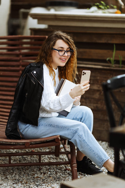 Portret van een jonge glimlachende blanke vrouw met behulp van mobiele telefoon, communicatie, chatten. Gelukkige vrouwelijke holding smartphone, online winkelen of studeren - Foto, afbeelding
