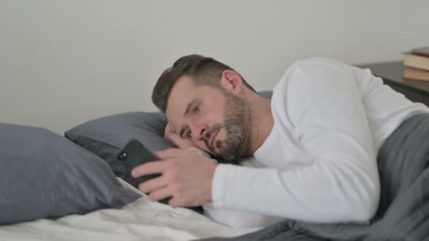 A férfi okostelefont használ, miközben alszik az ágyban - Felvétel, videó