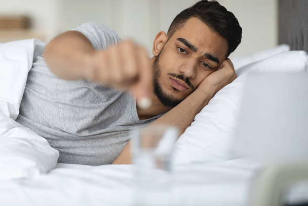 Kranker Araber steckt Pille ins Wasserglas, während er im Bett liegt - Foto, Bild