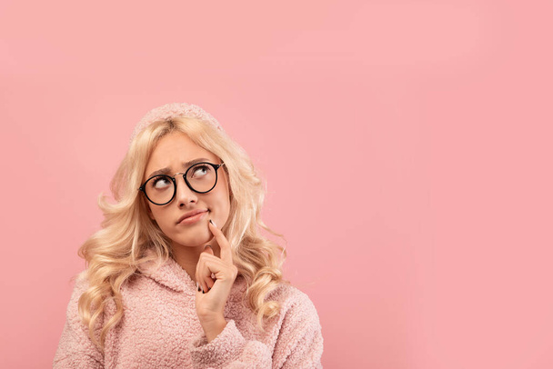 Στοχαστική ξανθιά γυναίκα με γυαλιά κοιτάζοντας χώρο αντιγραφής, στέκεται πάνω από ροζ φόντο στούντιο, banner design - Φωτογραφία, εικόνα