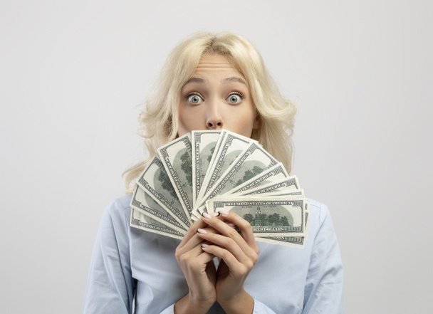 Empresaria impactada cubriéndose la cara con dinero, escondiendo la cara detrás de un ventilador de dinero en efectivo en sus manos, fondo claro - Foto, imagen