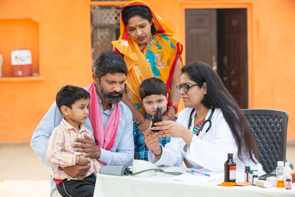 Молода індійка-доктор з сільською сім'єю дає медицину на вулиці сільської лікарні, концепцію державного табору охорони здоров'я. Батьки з двома синами отримують медичну допомогу та підтримку від педіатра. - Фото, зображення
