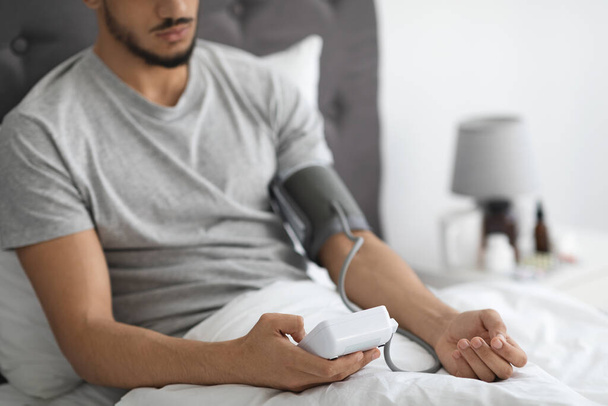 Arabimies istuu sängyssä, tarkistaa verenpainetta Upper Arm Monitor - Valokuva, kuva