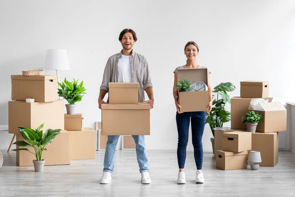 Pleased millennial caucasian male and female carry boxes and plants in room interior and enjoy moving at own home - Photo, Image