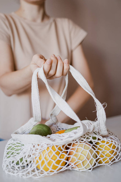 The girl is holding an eco-aware handbag with a variety of fruits. Ecological shopping bag. Avocados, lemons, peaches, pears, oranges. - Photo, image