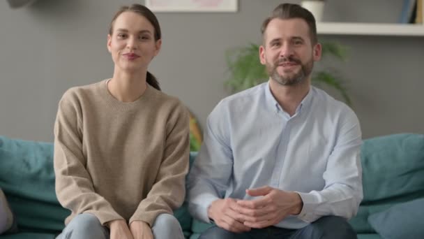 Couple souriant à la caméra assis sur le canapé  - Séquence, vidéo