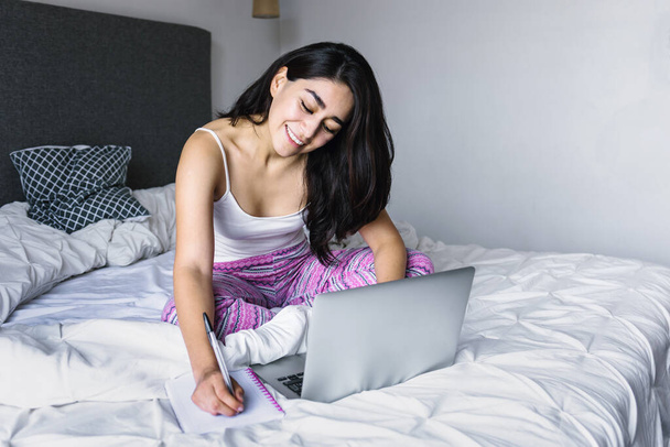 chica latina con computadora y cuaderno en la cama en casa en México América Latina - Foto, imagen